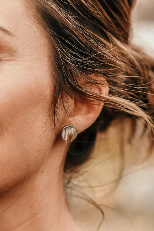 A close-up image of a person's ear wearing a silver-colored stud earring made from brown and white hair on cowhide.